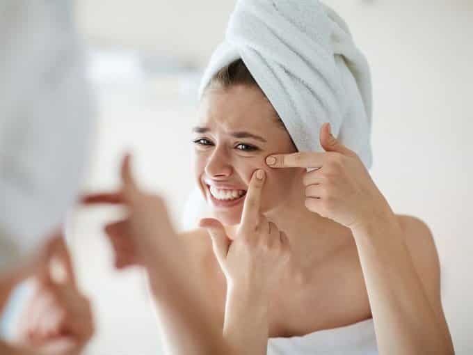 woman looking at acne zit in mirror