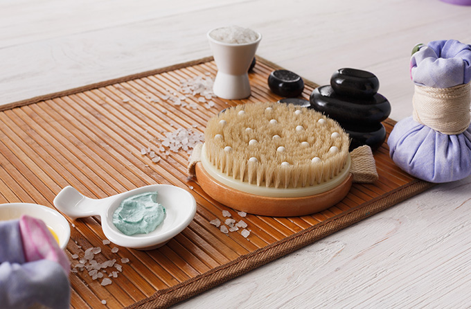 Spa treatment, body care and aromatherapy background. Massage brush, zen black stones, aroma salt, herbal balls, other details and accessories for wellness and beauty on bamboo mat